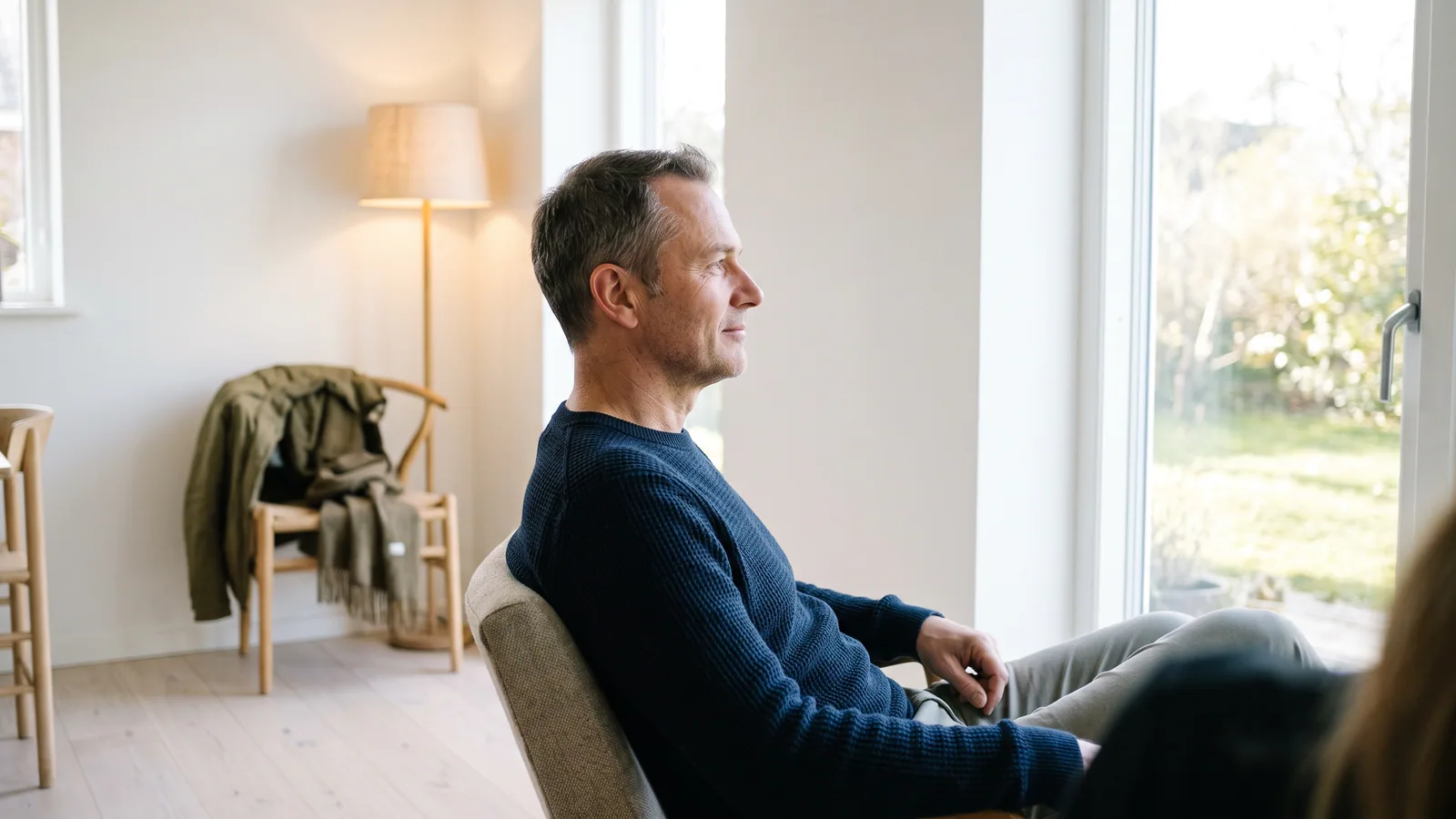 En rolig mann i femtiårene sitter avslappet ved et vindu og ser ut, uten bekymring
