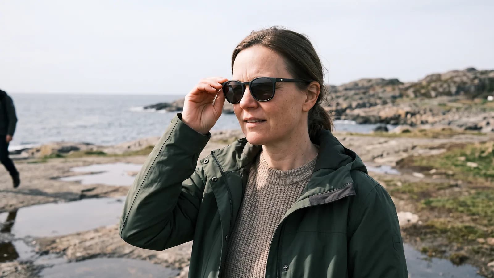 En kvinne i 40-årene tar på seg solbriller med UV-filter på en solrik dag ved kysten, vern mot UV-stråler som kan gi pingvekula.
