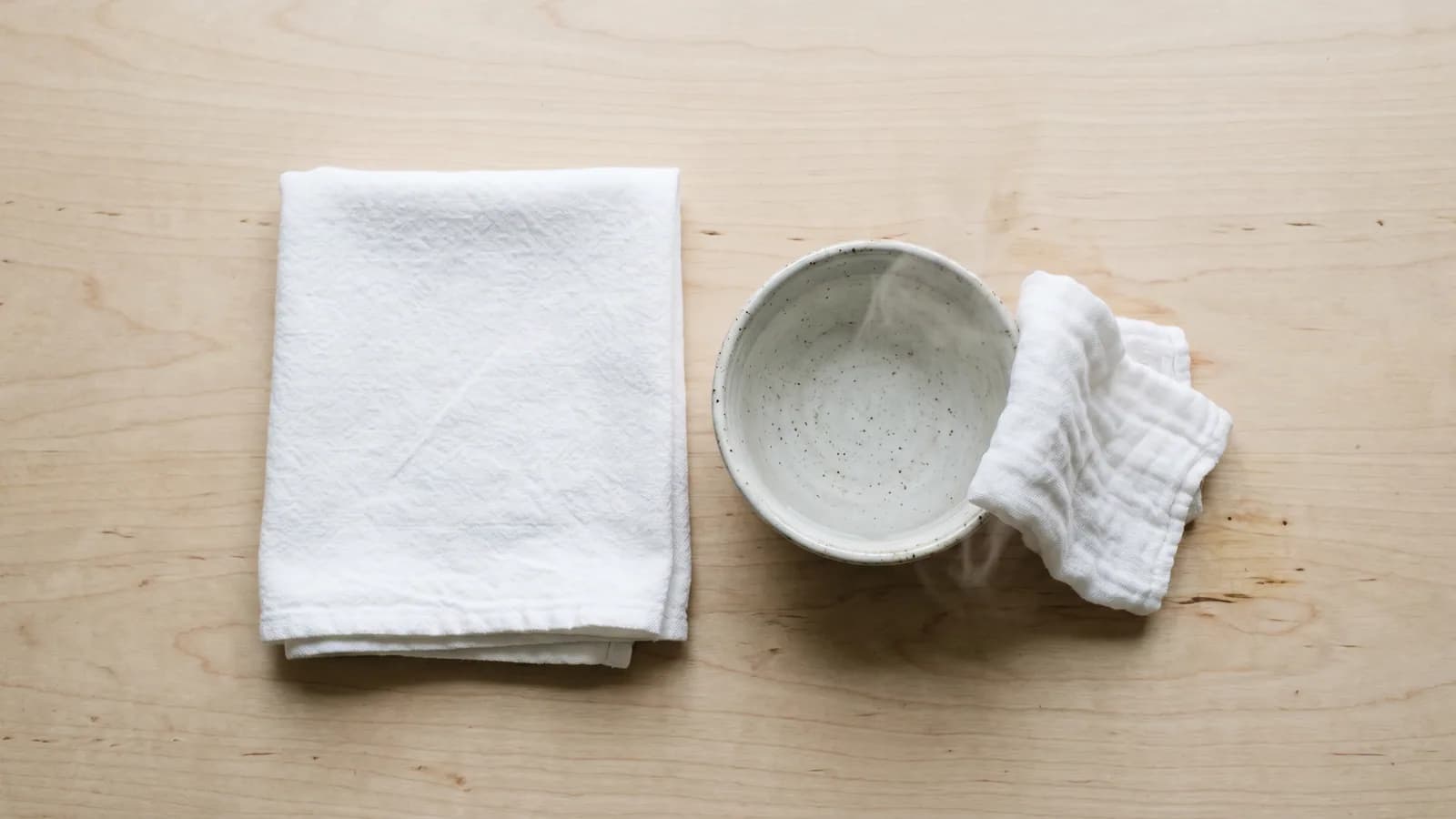 En ren sammenbrettet klut ved siden av en skål med varmt vann, sett ovenfra